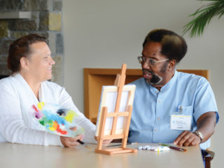 Leon Wallace in a blue shirt talking with a woman in a white shirt in front of a paint canvas.